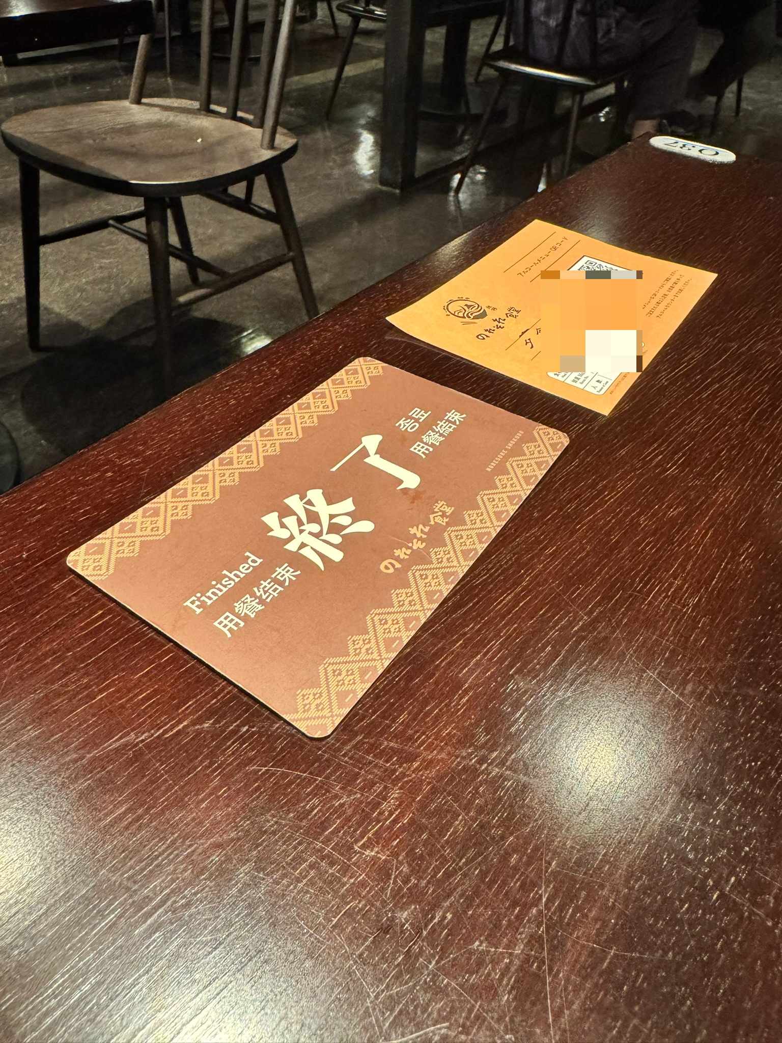 식사가 끝났음을 알리는 '종료(Finished)' 카드가 놓인 짙은 갈색 나무 테이블. 옆에는 QR코드가 인쇄된 노란색 안내문과 리조트 캐릭터가 그려진 식사권이 놓여 있음.