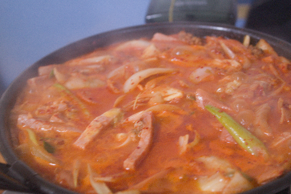 고춧가루가 있어 매워보이는 부대찌개. 햄, 양파, 김치가 보인다.