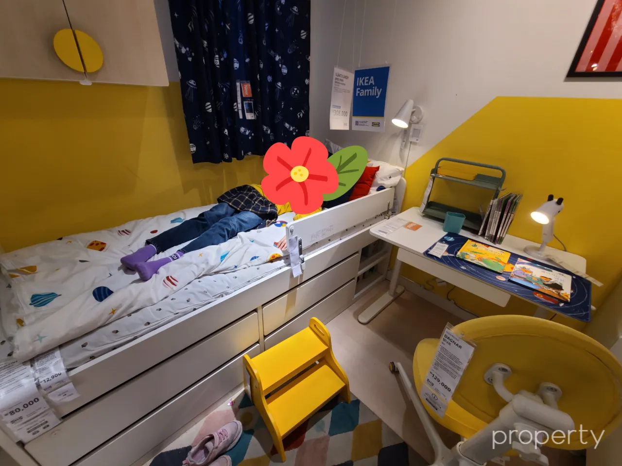 이케아쇼룸-노란색벽지-알록달록한이불-서랍형침대에누운아이-침대옆에흰색책상-책상위책과스텐드-노란색의자