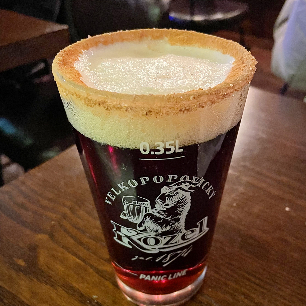 중앙에-코젤다크-맥주가-담긴-맥주잔이-확대되어-있고-거품-주변에-시나몬-가루가-뿌려져-있습니다.
