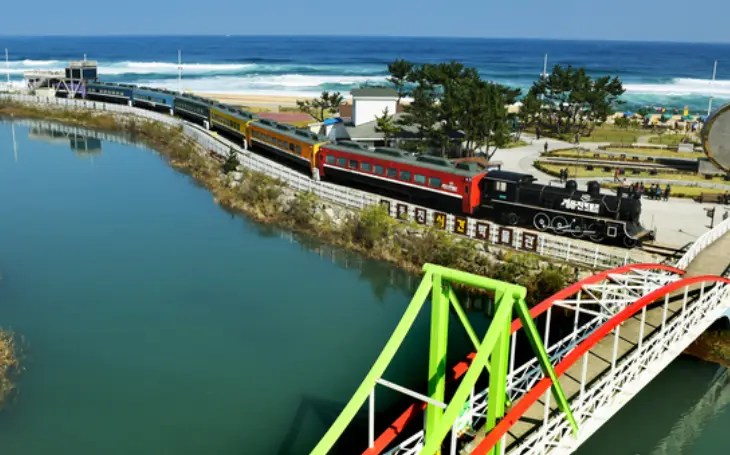 윗쪽 바닷가와 아랫쪽 호수 사이로 알록달록한 기차가 지나가는 모습