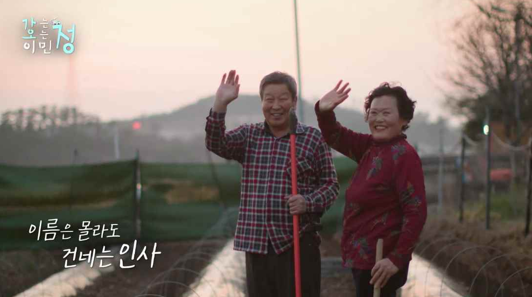 중년 부부가 환하게 웃으며 손을 흔드는 장면에 이름은 몰라도 건네는 인사 자막이 있는 스틸컷