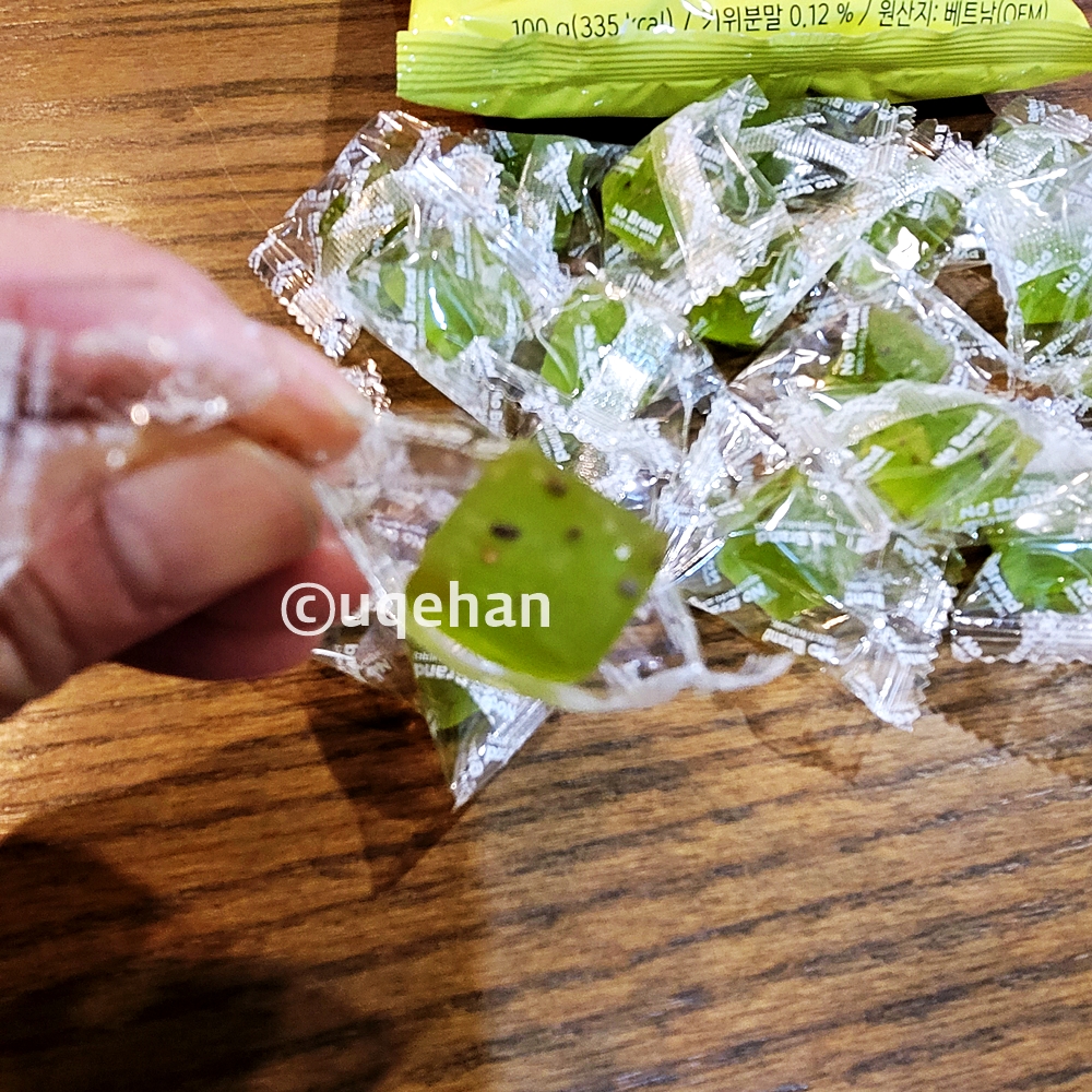 노브랜드 키위 젤리가 테이블 위에 올려져 있고, 개별포장된 젤리를 포장을 뜯어 하나 들고 있다.