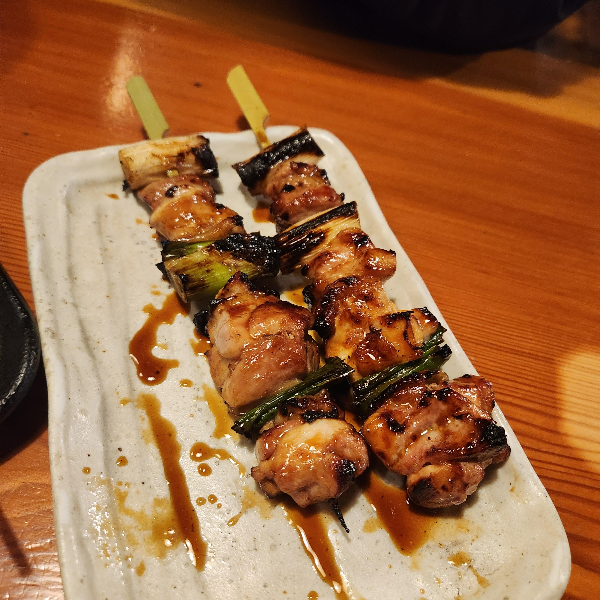 테이블 위에 간장 소스가 발라진 닭꼬치 구이가 있다.