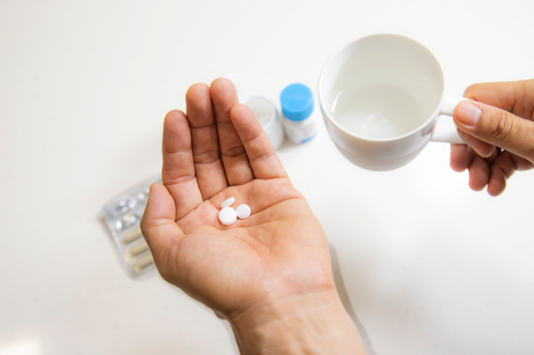 한손에는 물컵이 왼손에는 알약이 들려있다.
