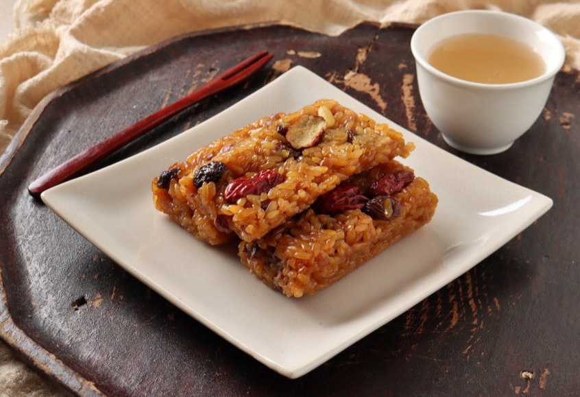 나무 갈판 위에 네모나고 하얀 사기그릇에 약밥 3덩이가 놓여 있고&#44; 그 옆에는 나무 포크가 있고&#44; 그 옆에는 사기 찻잔에 차가 담겨 있는 사진