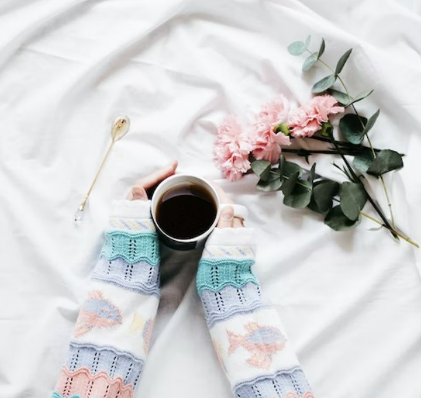 머그컵에 담겨있는 커피를 니트를 입은 여성이 두 손으로 잡고 있다.