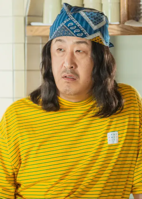 닥터슬럼프-
흰색 벽의 주방 앞 노란색 긴팔티를 입고 머리에 파란두건아래 곱슬머리가 어깨가지 내려오는 공태선이 옆을 바라보는 모습