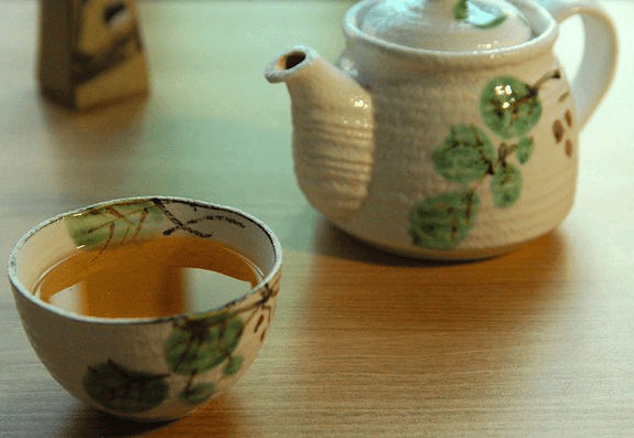 하얀 도자기 주전자가 있고 왼쪽에는 연갈색의 보이차가 가득 담긴 하얀 도자기 찻잔이 있다.