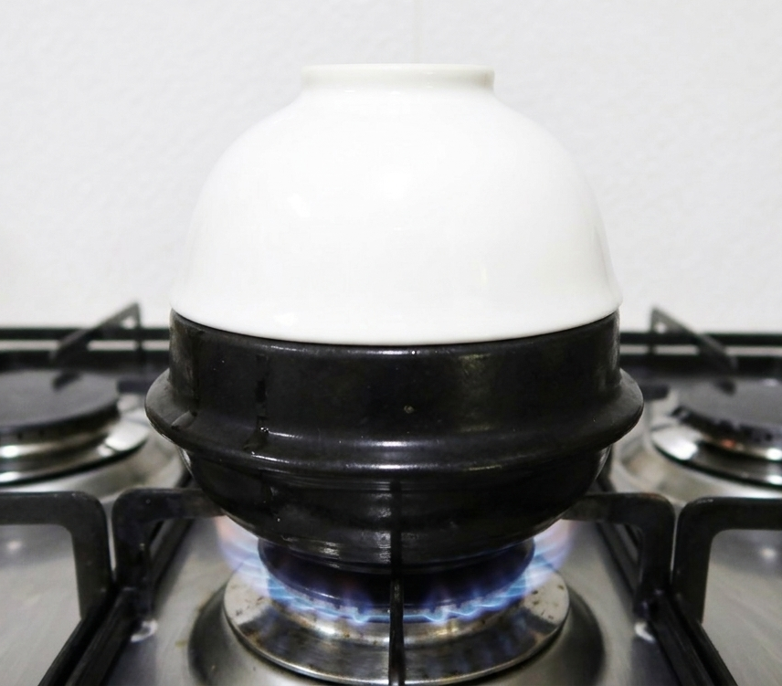 가스레인지 화구 위 검은색 뚝배기에 흰색 공기를 거꾸로 엎어놓은 폭탄 계란찜 조리 과정 사진.