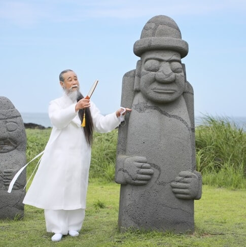 제주도에서 돌하르방 옆에 부채 들고 서 있는 천공