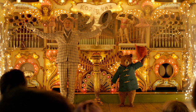 패딩턴 2의 스틸컷 속 파란색 더플코트를 입고 빨간보자를 벗어 인사하는 패딩턴