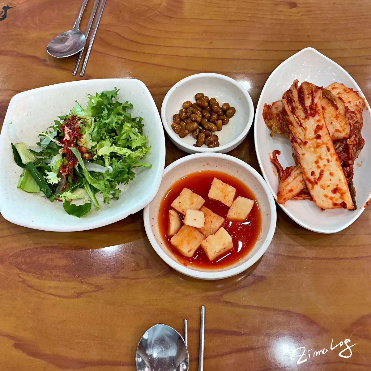 테이블 위에 밑반찬인 김치, 깍두기, 치커리 겉절이 등이 있음