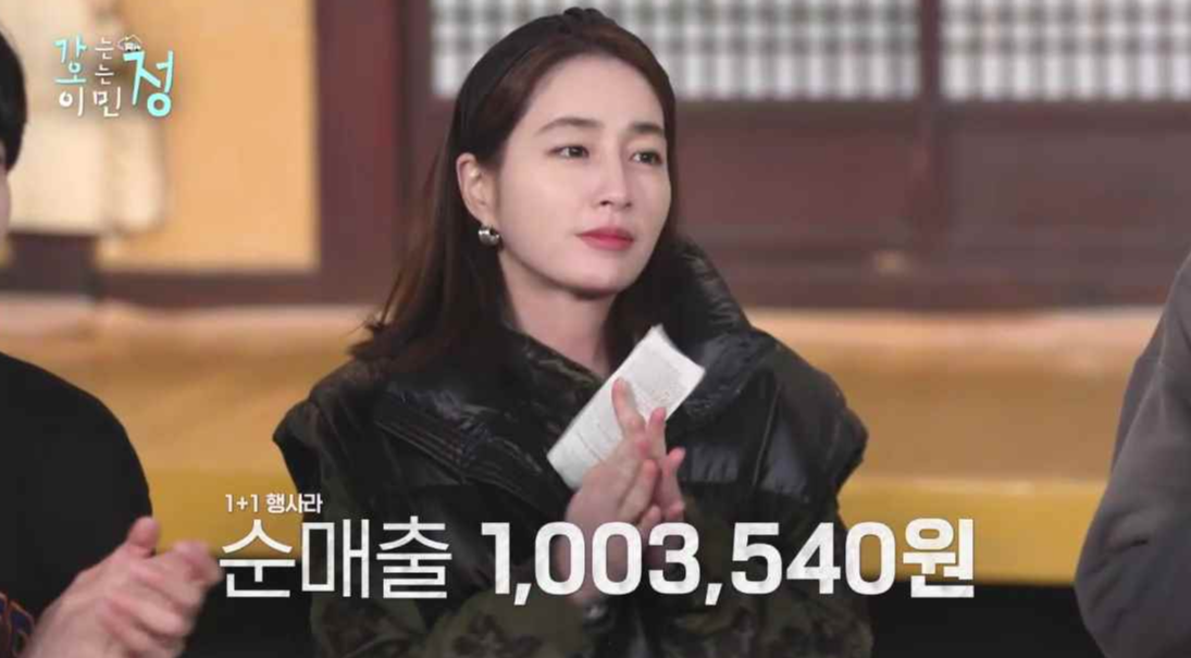 이민정이 박수치는 장면에 1+1 행사라 순매출 1,003,354원 자막이 있는 스틸컷