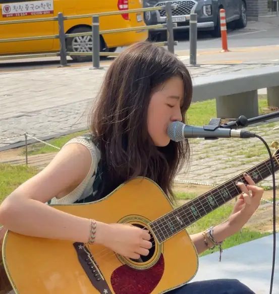 싱어게인3- 거리에 앉아서 연한 갈색 통기타를 치며 머리카락을 길게 늘어뜨린채 나시옷을 입고 스탠딩마이크에 입을 대고 노래한 68호