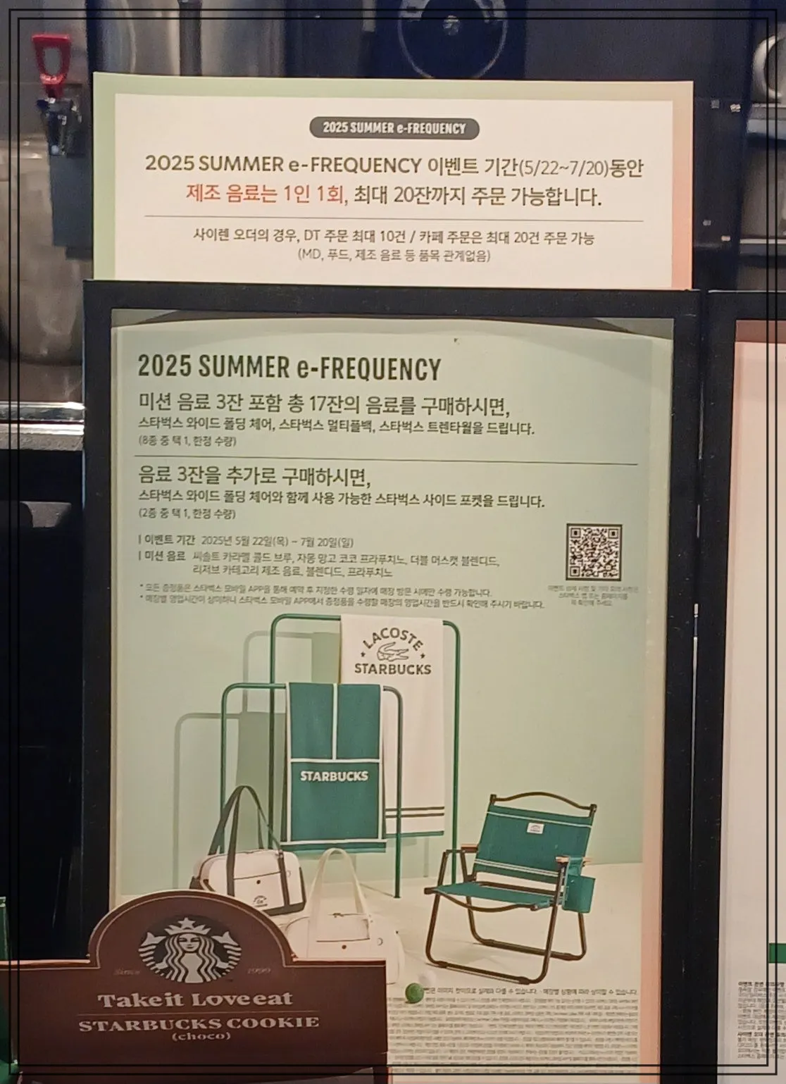 스타벅스-매장-카운터에-2025-SUMMERe-FREQUENCY-이벤트-안내판이-전시되어-있다-상단에는-이벤트-기간이-5월-22일부터-7월-20일까지이며-제조-음료는-1회-최대-20잔까지-주문-가능하다는-내용이-적혀-있다-하단에는-미션음료-3잔-포함-총-17잔-구매-시-사은품을-증정하며-추가로-3잔을-더-구매하면-사이드-포켓을-받을-수-있다는-내용이-상세히-적혀-있다