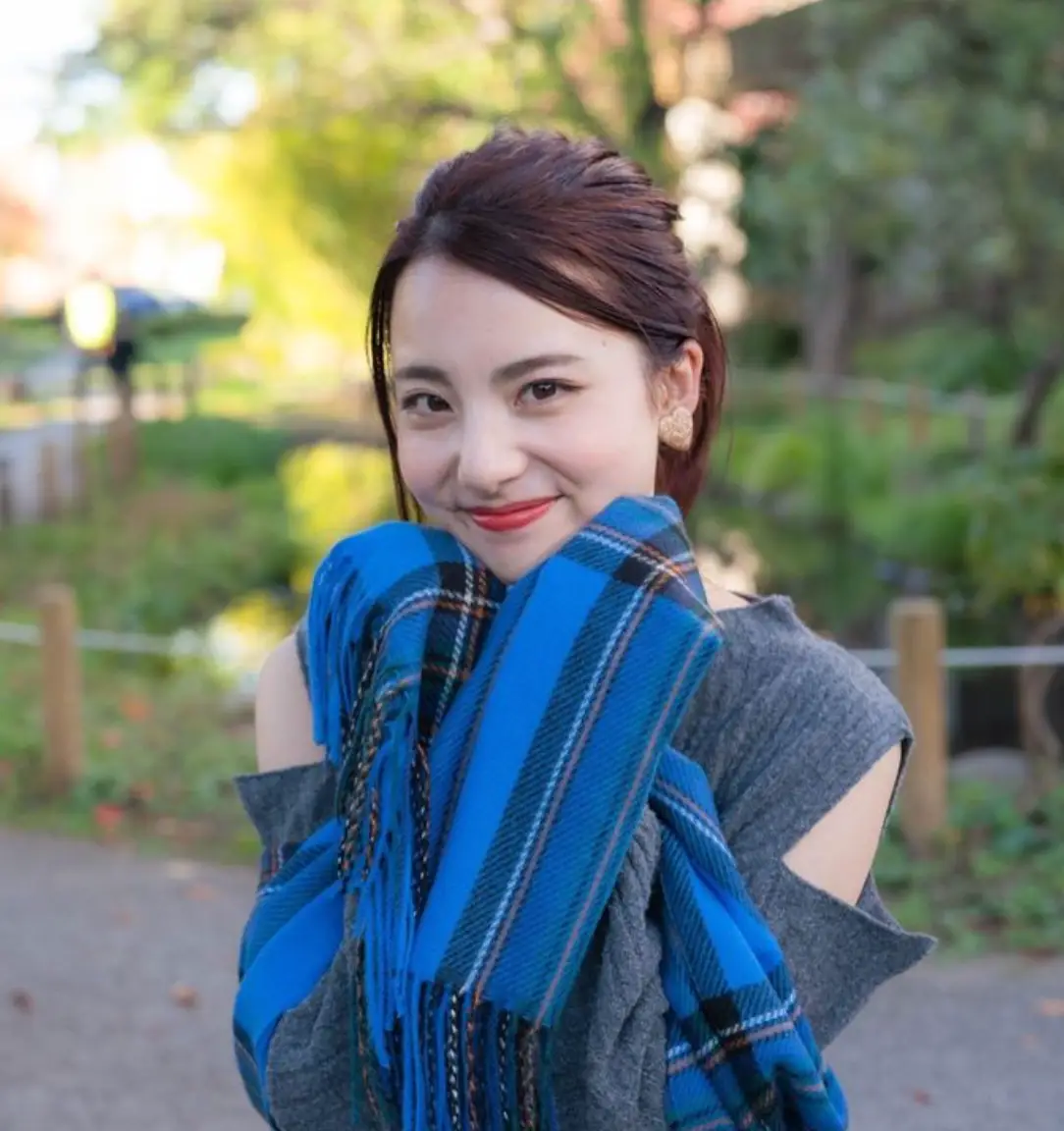 한일-초록색 나무가 있는 숲을 뒤로한채 회색옷을 입고 파란 목도리를 든채 미소짓는 카노 미유