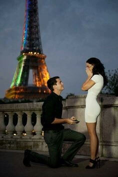 파리-에펠탑을-멀리두고-남자가-한쪽-무릎을-꿇고-반드를-들고-흰-옷을-입은-여성에게-프로포즈하는-장면