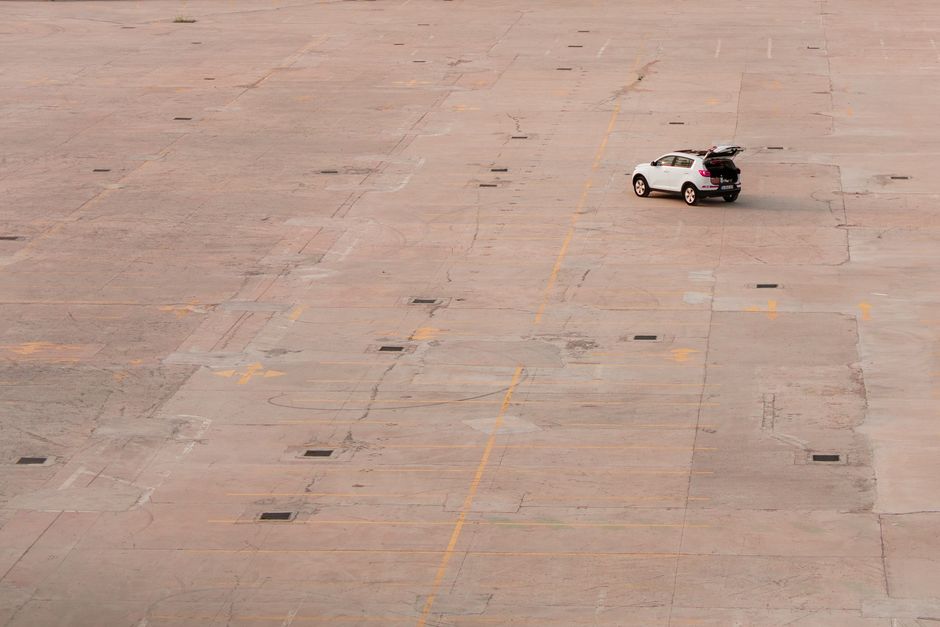 A white SUV with open trunk on an empty concrete parking lot captured from above.