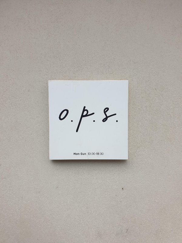 회색 벽면에 정사각 간판에 o.p.s라는 글자가 쓰여있다.