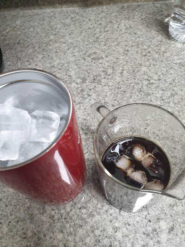 빨간 텀블러에 얼음이 담겨 있고 비커에는 추출된 커피가 얼음과 함께 담겨 있다.