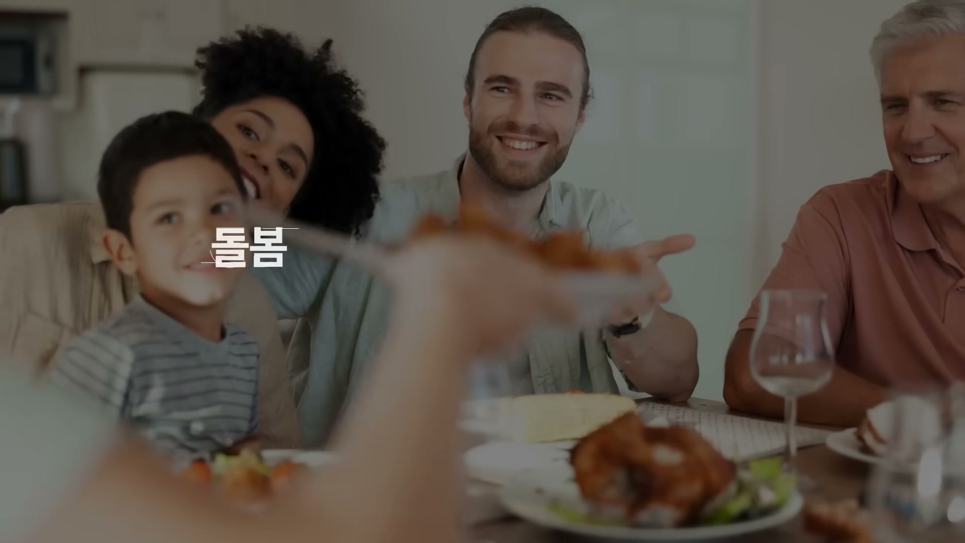 다인종 가족 구성원들이 식탁에 둘러앉아 함께 식사하며 웃는 장면. 화면에 돌봄이라는 단어가 떠 있다.