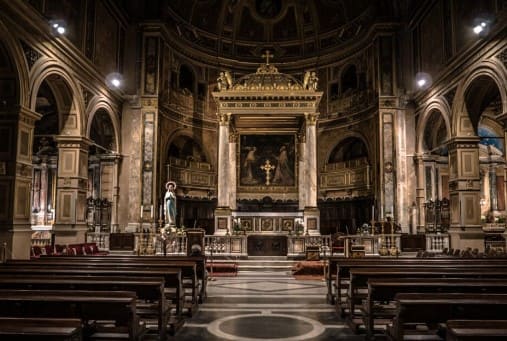 어두운 조명의 교회 안 의자들과 십자가가 멀리 보인다