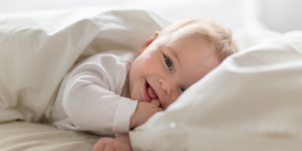침대 이불 밑에서 해맑게 웃고 있는 아기.