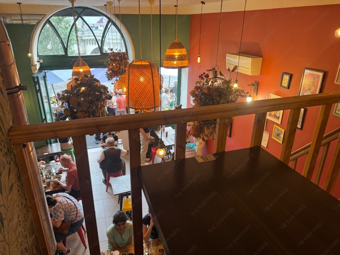 The cozy interior of Hanoi 1988 viewed from the upper floor featuring warm orange walls and traditional woven lanterns ❘ L'intérieur chaleureux de Hanoi 1988 vu de l'étage supérieur avec des murs orange et des lanternes traditionnelles en osier