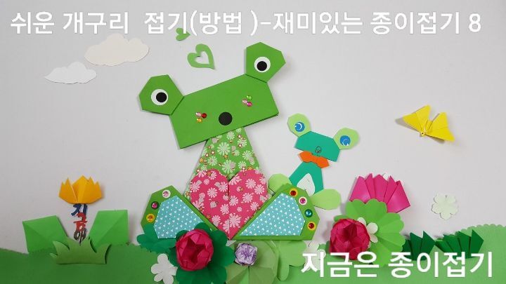 시니어, 실버 종이접기 활동에 즐거움을 줄 수 있는 쉬운 개구리 접기(방법)으로 접은 개구리가 꽃이 핀 들판에 두 마리가 앉아 있는 모양입니다.