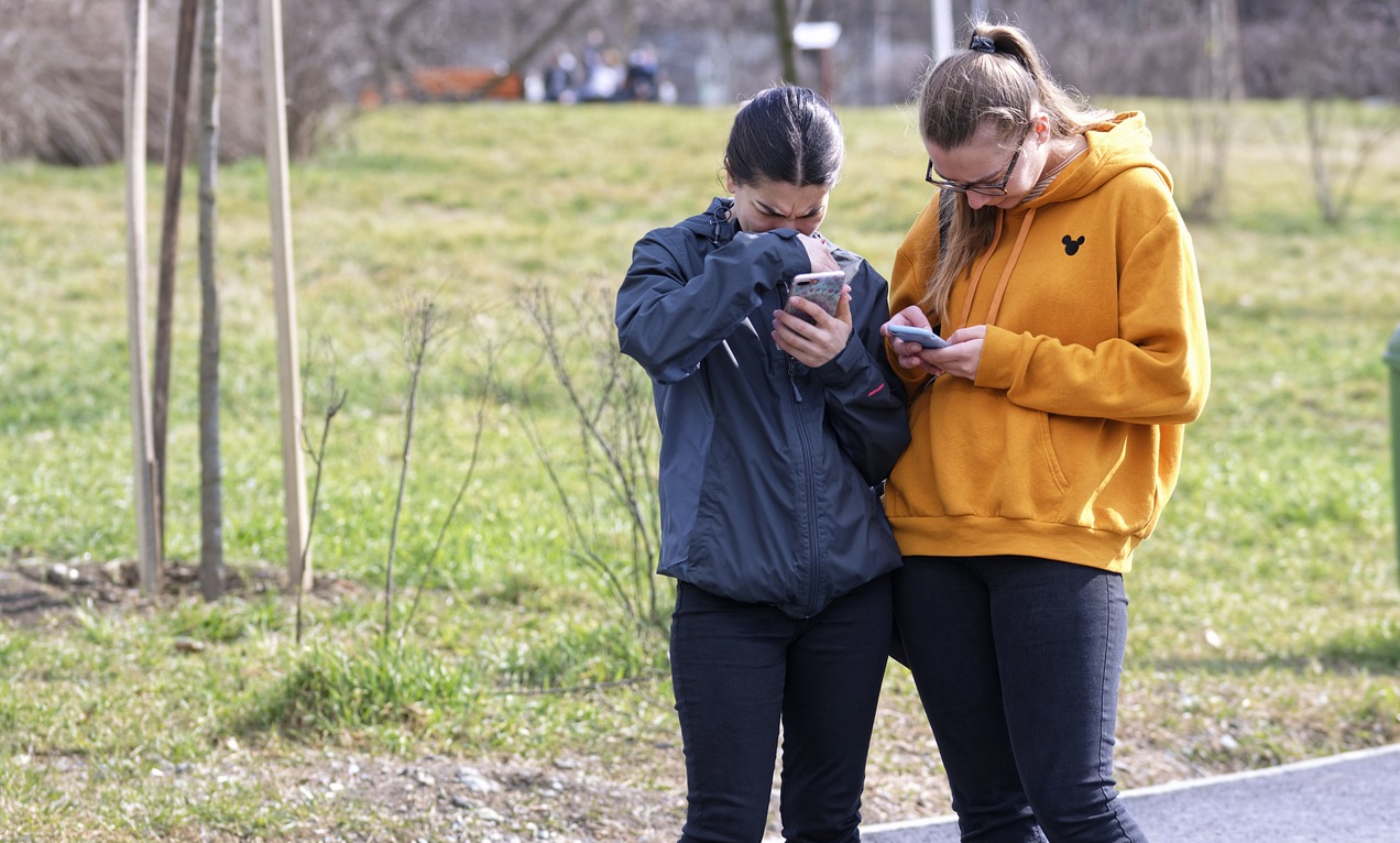 두명의-여성이-각자의-휴대폰을-들여다-보고-서있다.