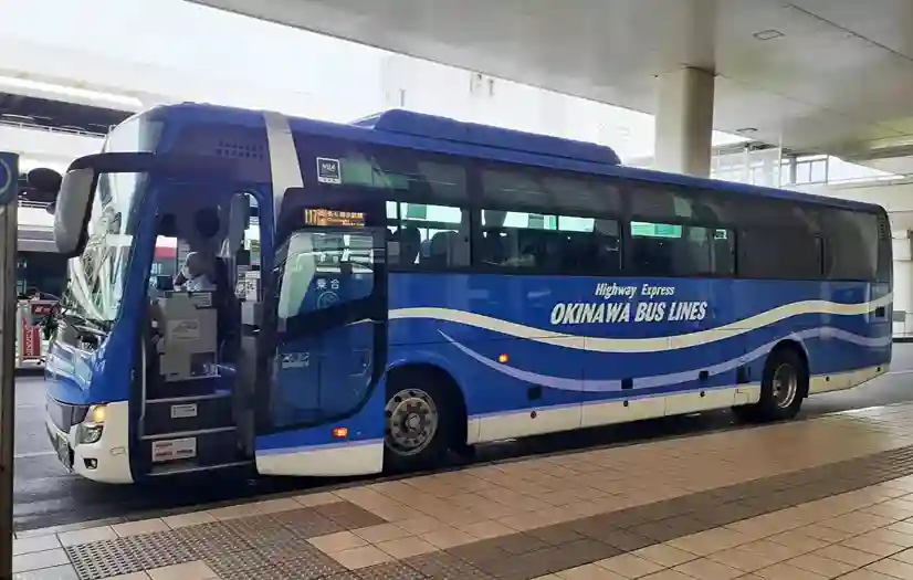 오키나와 버스 라인(OKINAWA BUS LINES)이 적힌 파란색 츄라우미 수족관 행 고속버스가 버스 정류장에 정차하여 승객이 탑승하는 모습.