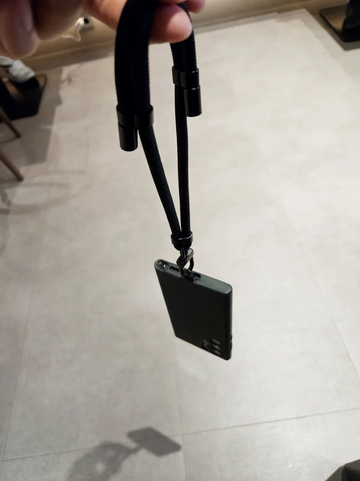 핸드폰-도난방지-스트랩-줄이 연결된-휴대폰을-허공에-손가락으로-들고있음