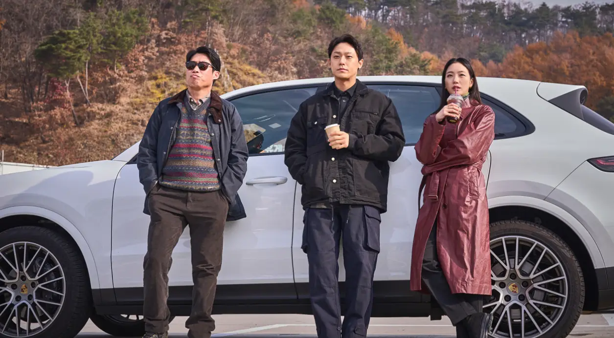 파묘- 흰색 자동차를 뒤로하고 서있는 선글라스 낀 유해진과 코피를 들고 있는 이도현, 김고은