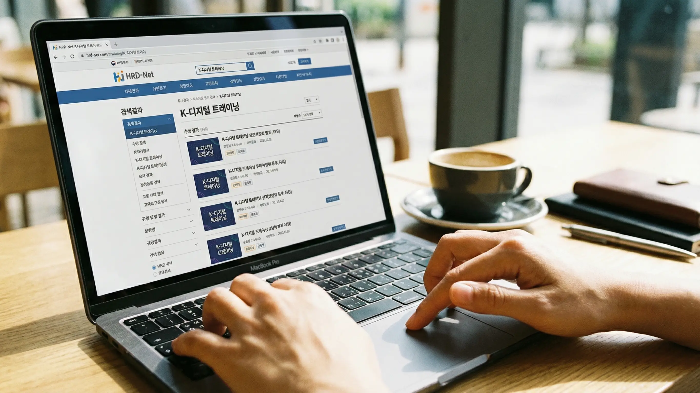 노트북 화면에 HRD-Net 홈페이지를 띄워놓고 K-디지털 트레이닝 과정을 검색하는 손 클로즈업