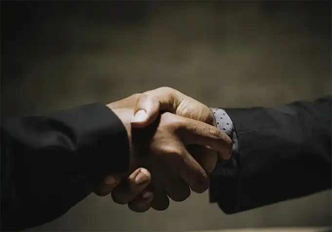 양복을 입은 두 사람이 악수를 하고 있는 모습이 클로즈업 되어있다.