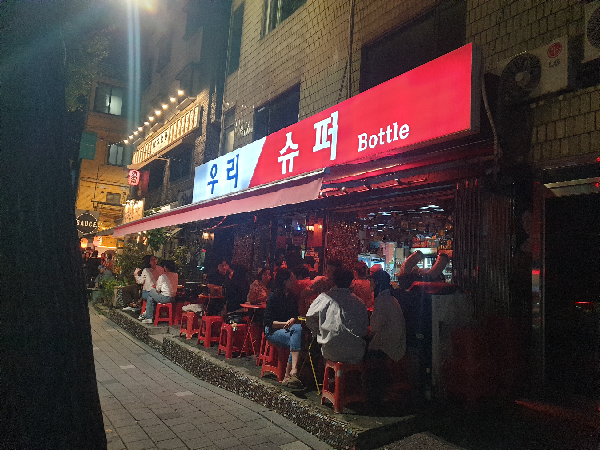 우리슈퍼의 간판이 빛나고 있다. 외부 좌석에는 손님들로 가득하다.