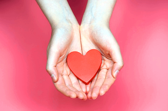 진분홍색 바탕화면 위에 여자의 두 손이 펼쳐져있고 그 안에는 붉은 하트가 담겨있다.