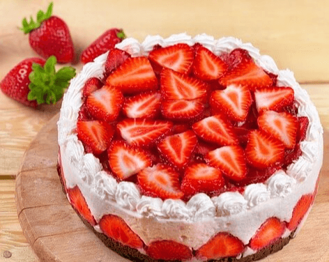 나무 탁자 위에 동그란 딸기 생크림 케이크가 있고 탁자 위에는 딸기 3개가 있다.