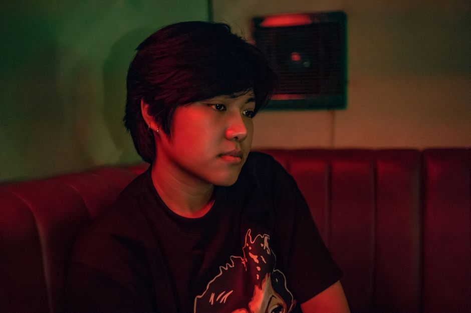 A young person sits thoughtfully in a dimly lit room, creating a moody atmosphere.