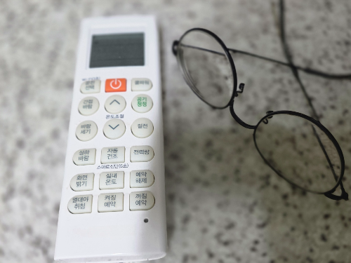 에어컨 리모컨과 돋보기안경으로 전기요금 절약을 위한 냉방 관리 모습