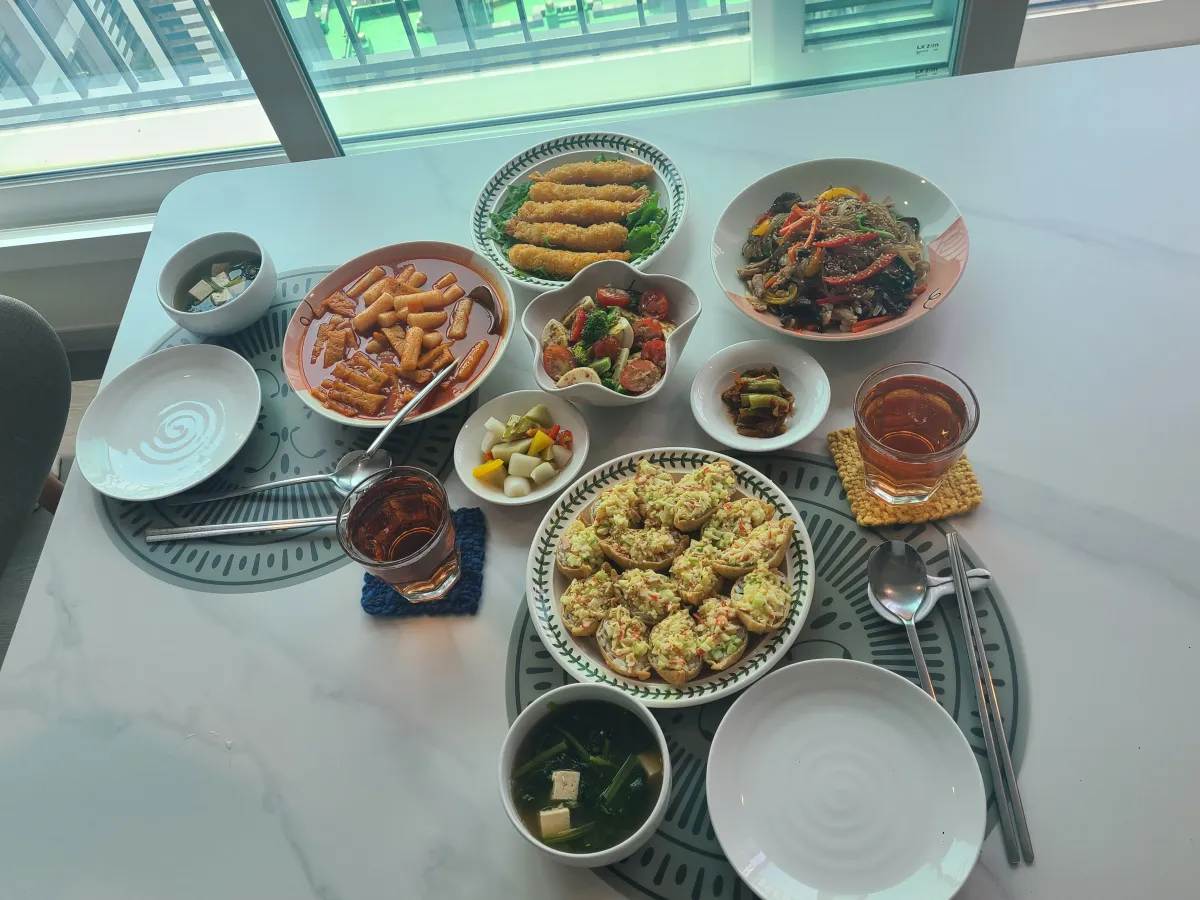 화이트대리석테이블위에-2인식사세팅-새우튀김-잡채-떡볶이-크래미샐러드유부초밥-샐러드-피클-오미자에이드