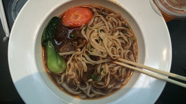 맛있는 우육면이 청경채, 당근, 고기 고명과 함께 하얀 그릇에 담겨있다. 그리고 젓가락이 그릇에 올려져 있다.