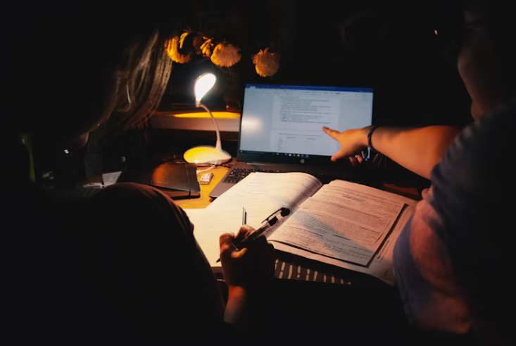 책상 위에 노트북과 문서를 펼쳐놓고, 두 사람이 함께 자료를 확인하며 손가락으로 화면을 가리키고 있다. 연말정산 또는 중요한 자료를 정리하는 모습이다.