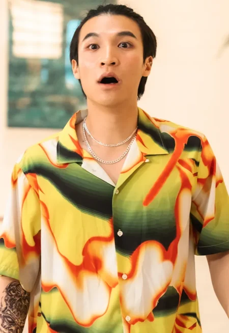 오렌지와 초록색의 화려한 셔츠에 은목걸이 두르고 멀리를 올백으로 넘긴 드라마 7인의 탈출의 홍만두 캐릭터