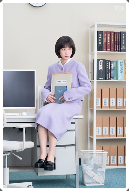 자료를 안고 책상위에 걸터앉아있는 배우