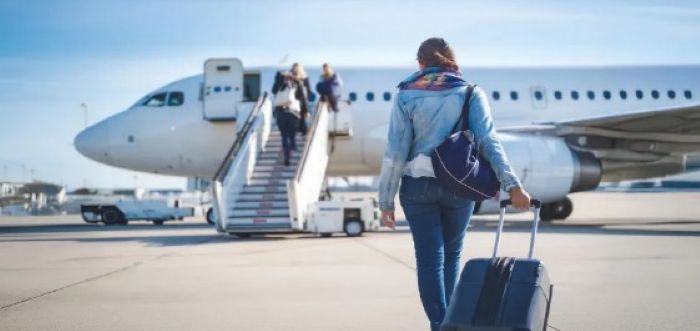 활주로에서 비행기를 향해 캐리어를 끌고 가는 여성 승객의 뒷모습&amp;#44; 비행기 탑승구 계단으로 올라가는 다른 승객들도 보임.