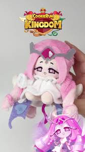 쿠키런-킹덤-로고가-상단에-있는-배경에서-한-손에-들린-이터널슈가쿠키-인형이-화면-중앙에-위치해있고-인형은-분홍색-머리카락과-왕관형-장식을-머리에-얹고-하얀-프릴-드레스를-입고있으며-보라색-하트-무늬의-방패와-검-모양의-장식이-달려있고-하단에는-게임-속-이터널슈가쿠키-캐릭터의-일러스트가-함께-배치된-구성