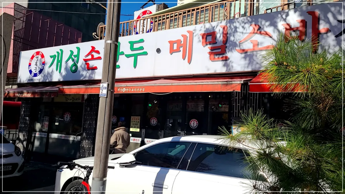 개성손만두의 건물모습, 간판에는 개성손만두 메밀소바라 적혀있음 빨간색 천막이 지붕처럼 덮고 있음.