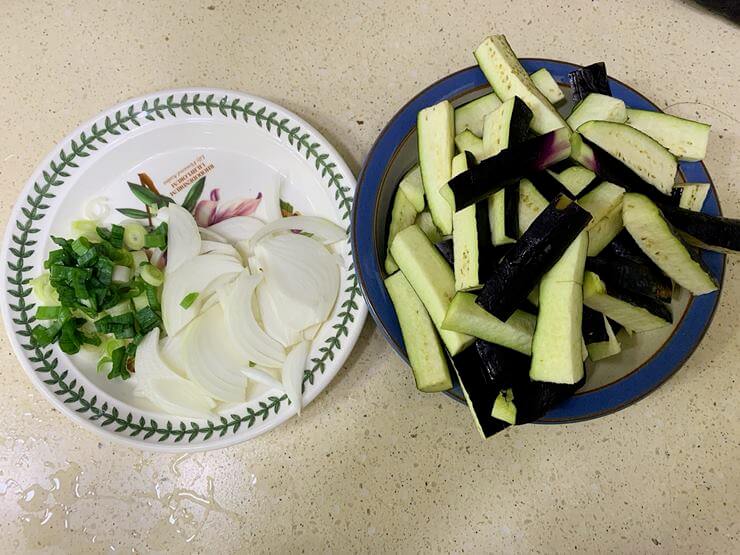 하얀색에 나뭇잎 테두리가 둘러진 접시와 하늘색 테두리가 둘러진 접시가 나란히 놓여있다.
왼쪽 하얀색 접시에는 채 썬 파와 양파가 담겨 있다.
오른쪽 접시는 손가락 크기로 자른 가지가 가득 담겨있다.